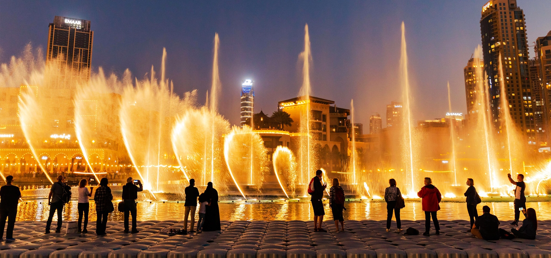 Tourists enjoying the Dubai Fountain Show and Lake Ride with Burj Khalifa illuminated in the background.