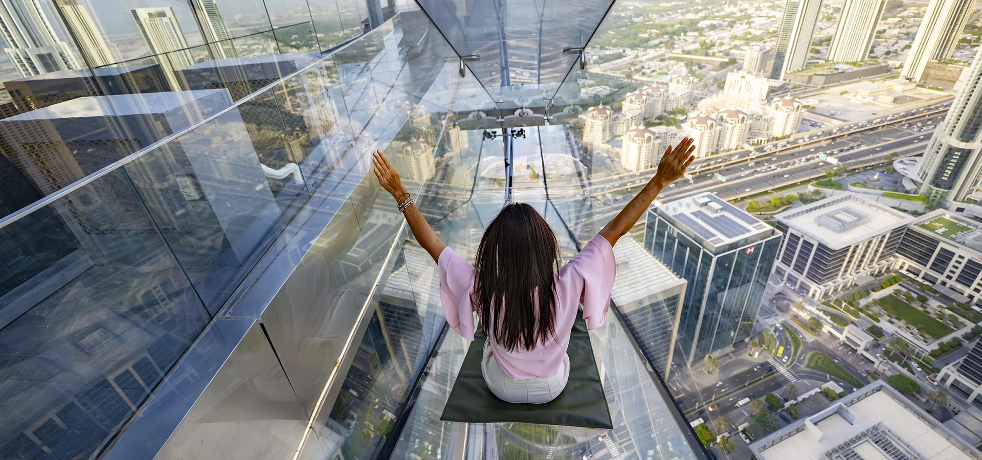 Tourists enjoying the glass slide and observation deck at Sky Views Dubai with a panoramic view of Burj Khalifa